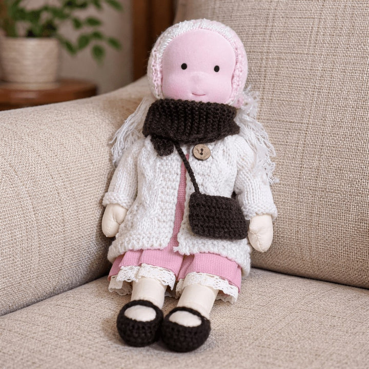 Handmade Waldorf-style cotton doll with a pink bonnet, brown scarf, white cardigan, pink leggings and a shoulder bag