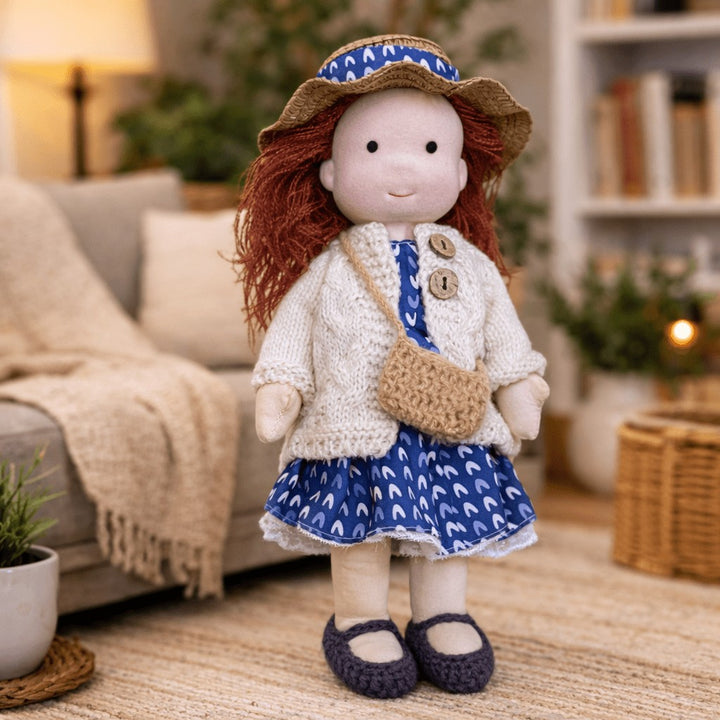 Handmade Waldorf-style cotton doll with auburn hair, a straw sun hat, a blue patterned skirt and a shoulder satchel