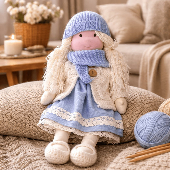 Handmade Waldorf-style cotton doll with a lilac knit hat and scarf and a blue lace skirt, beside a ball of yarn