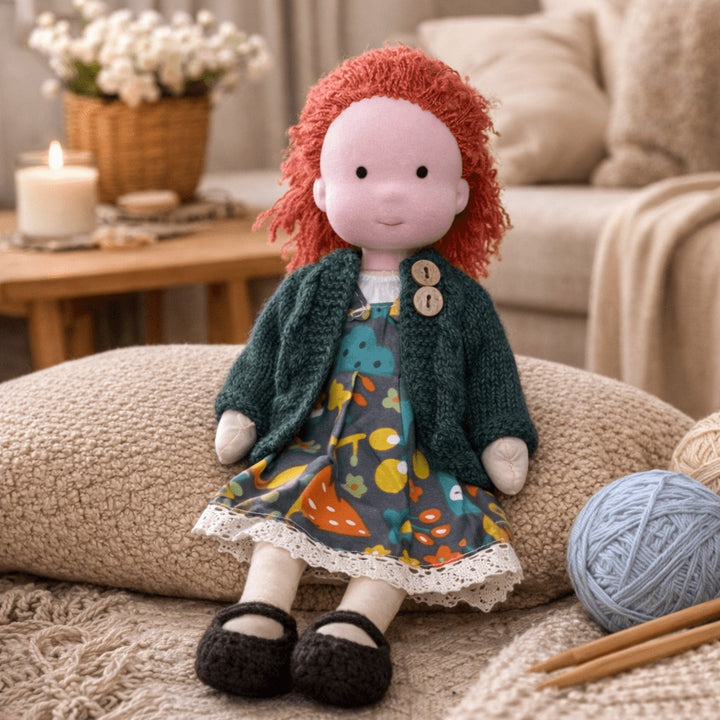 Handmade Waldorf-style cotton doll with red curly hair, a teal cardigan and a patterned skirt, next to knitting yarn