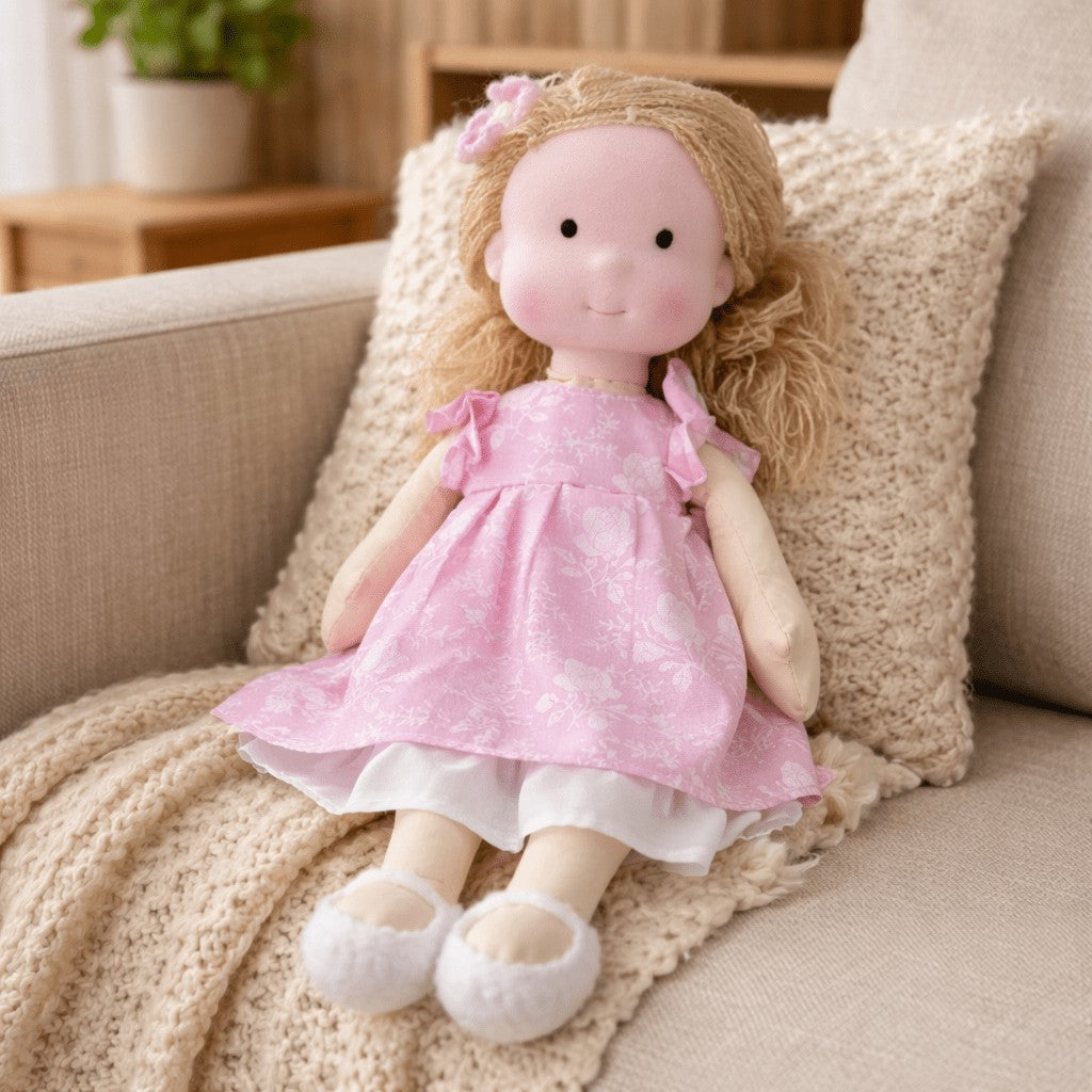 Handmade Waldorf-style cotton doll with blonde hair with a bow and a pink flutter-sleeve dress on a knit blanket