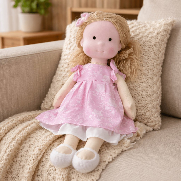 Handmade Waldorf-style cotton doll with blonde hair with a bow and a pink flutter-sleeve dress on a knit blanket