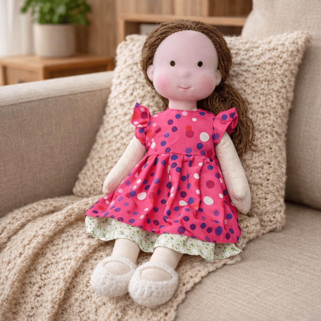 Handmade Waldorf-style cotton doll with brown hair and a pink polka-dot dress seated on a sofa