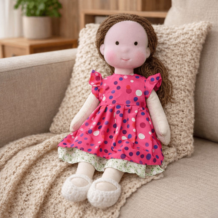 Handmade Waldorf-style cotton doll with brown hair and a pink polka-dot dress seated on a sofa