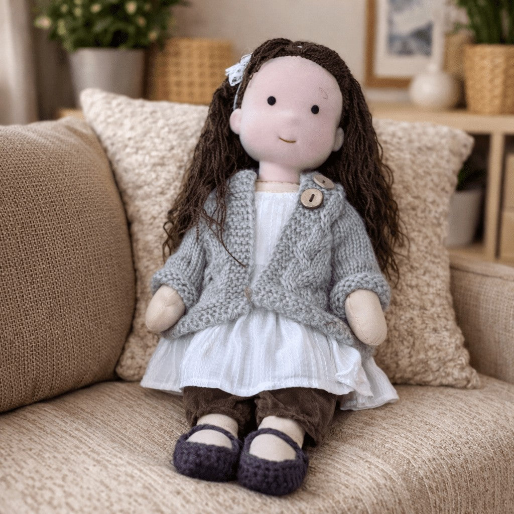 Handmade Waldorf-style cotton doll with dark brown hair with a clip, a gray knit cardigan and a white dress