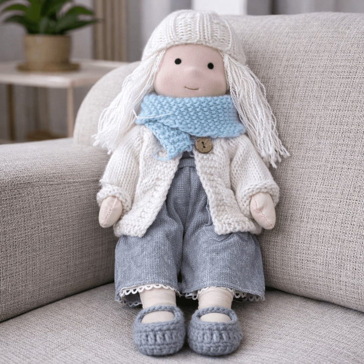 Handmade Waldorf-style cotton doll with long white hair, a blue scarf, a cable-knit cardigan and gray pants