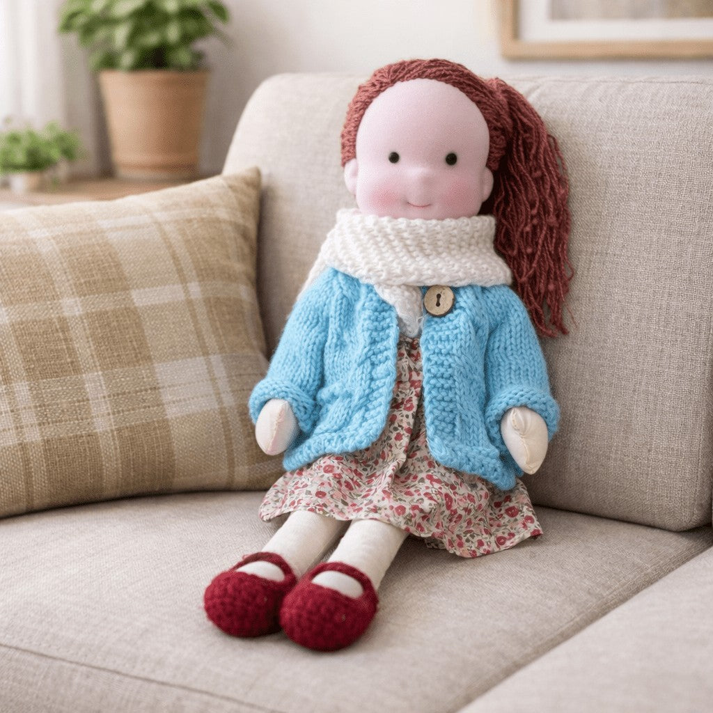Handmade Waldorf-style cotton doll with auburn hair, a cream scarf, light blue cardigan, floral skirt and red shoes