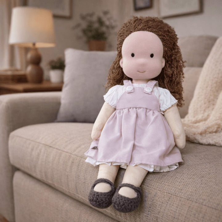 Handmade Waldorf-style cotton doll with brown curly hair, a lilac pinafore dress over a white blouse