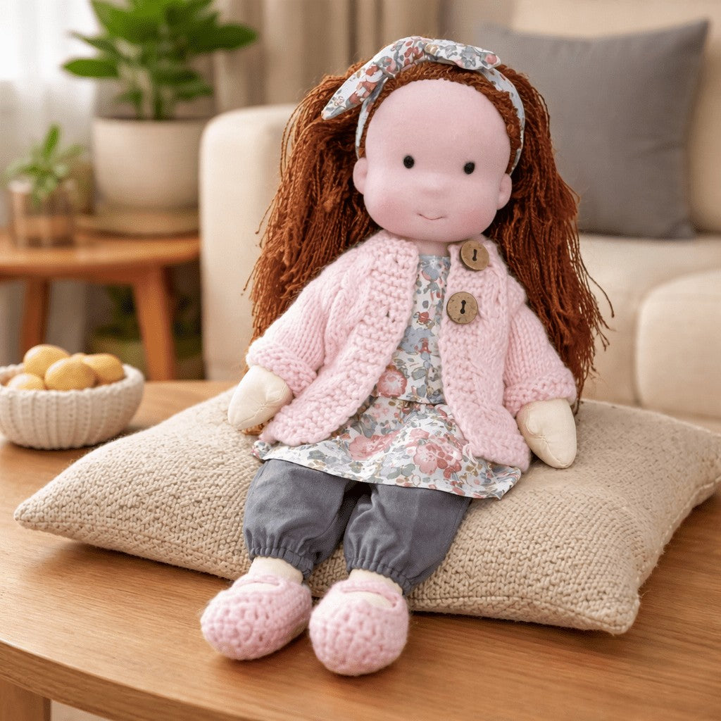 Handmade Waldorf-style cotton doll with auburn hair with a floral headband, a pink cardigan and gray pants