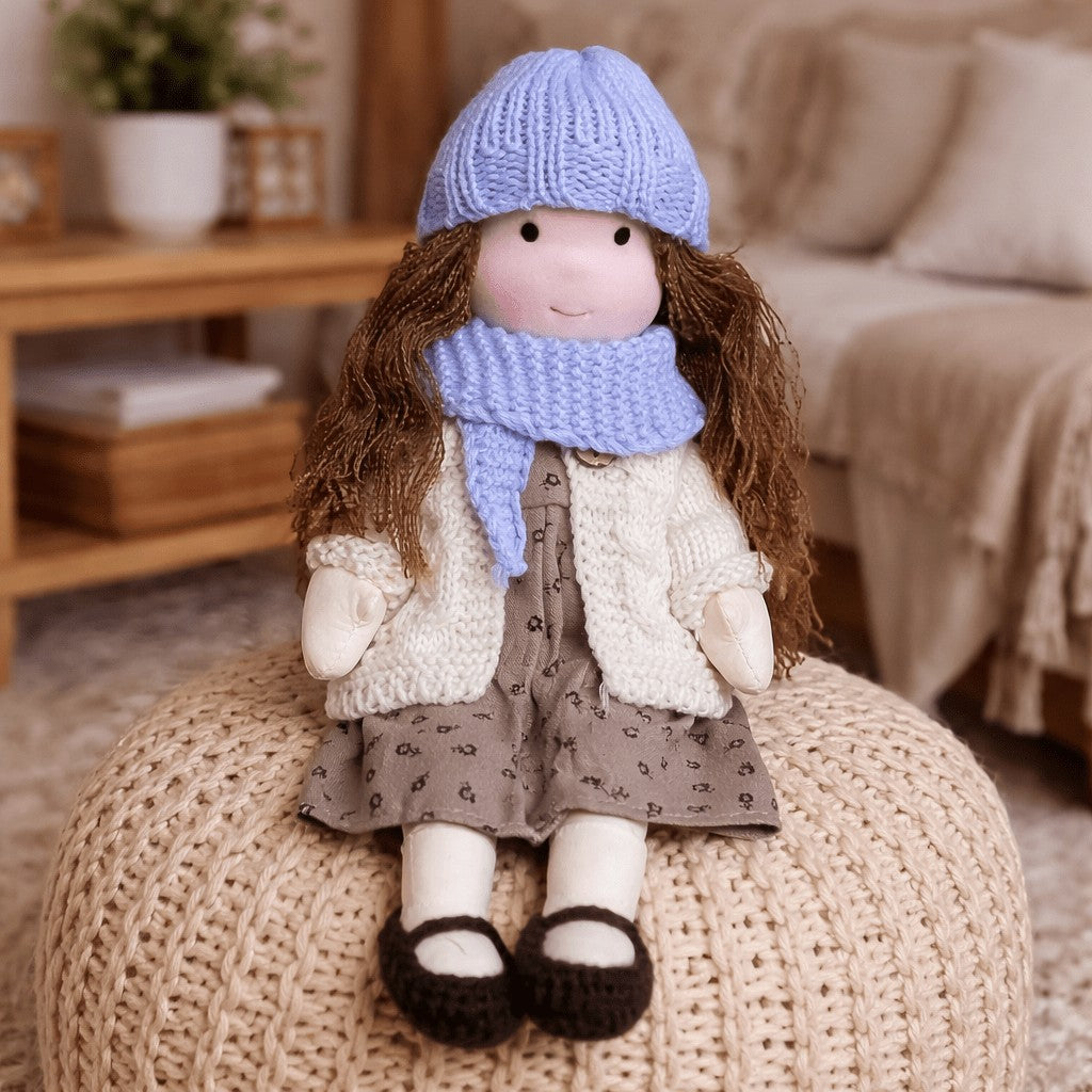 Handmade Waldorf-style cotton doll with brown hair, a blue knit hat, lilac scarf and a brown floral skirt on a knit pouf