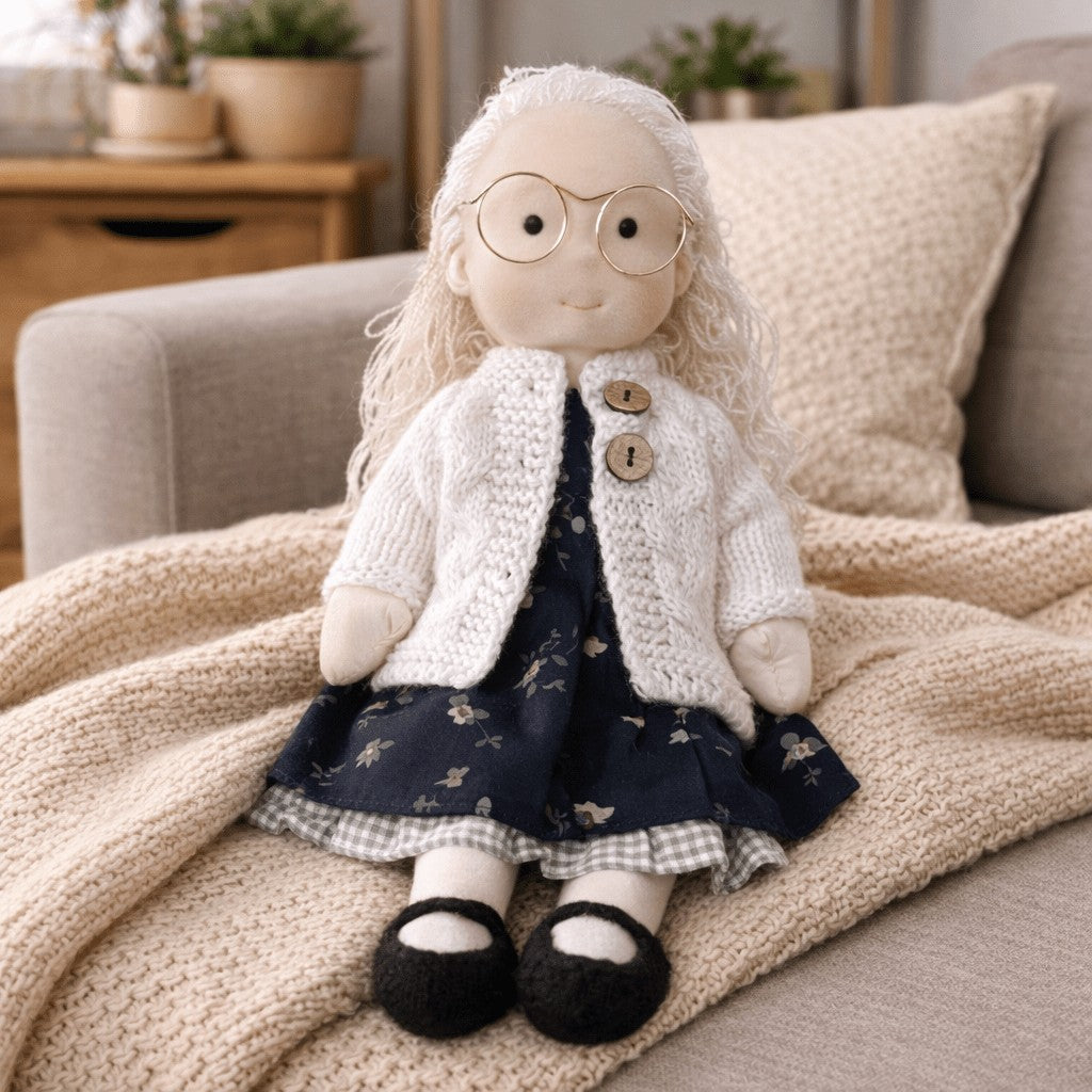 Handmade Waldorf-style cotton doll with white hair and round glasses, a cream bonnet and a navy floral skirt
