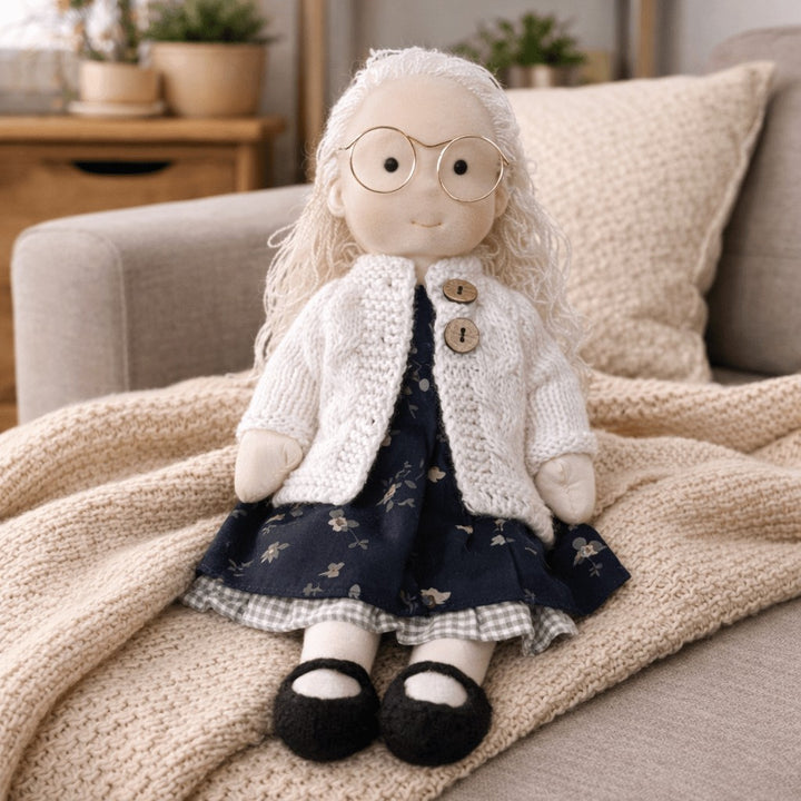 Handmade Waldorf-style cotton doll with white hair and round glasses, a cream bonnet and a navy floral skirt