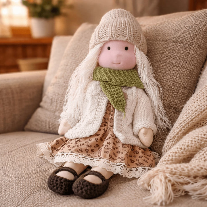 Handmade Waldorf-style cotton doll with long blonde hair, a cream knit hat, green scarf and a tan floral skirt